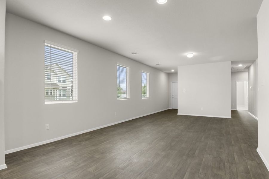 Image of a one-story home dining room with brown vinyl flooring, light grey walls, and windows