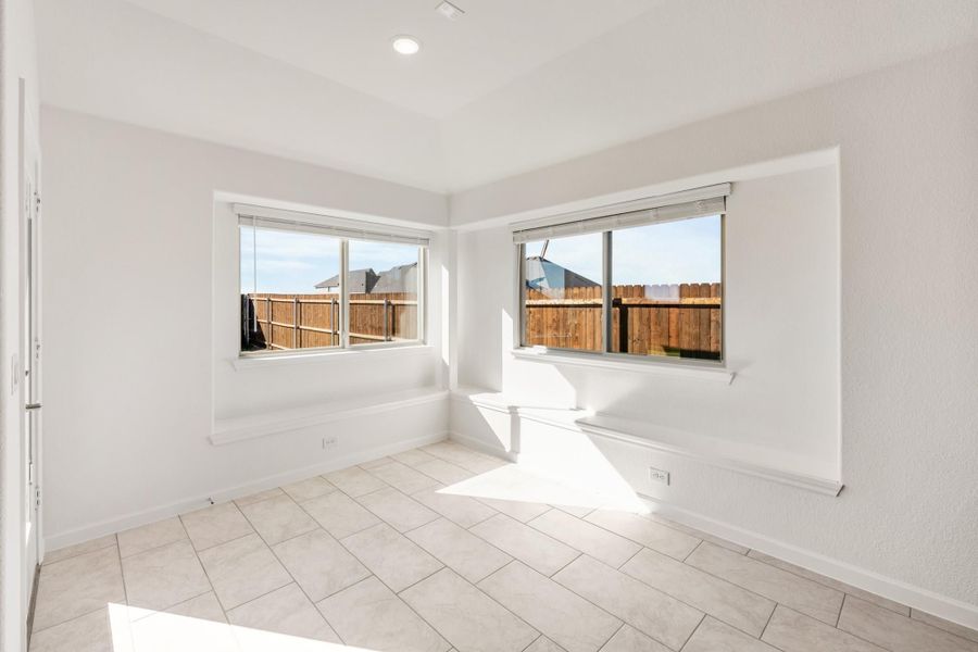 Empty room with white walls, tile floors, and two windows overlooking a wood fence backyard