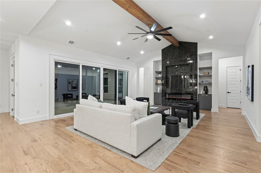 Living area with light wood finished floors, baseboards, visible vents, a premium fireplace, and vaulted ceiling with beams