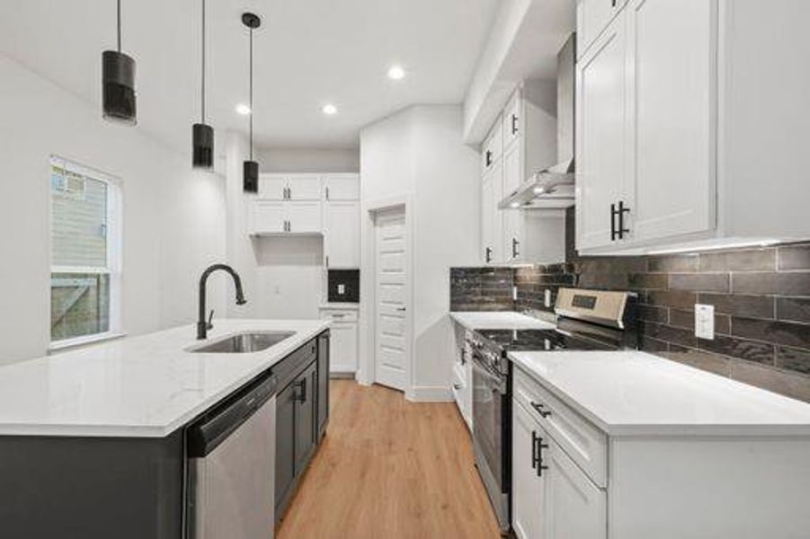 Kitchen featuring sink, wall chimney range hood, pendant lighting, white cabinets, and appliances with stainless steel finishes