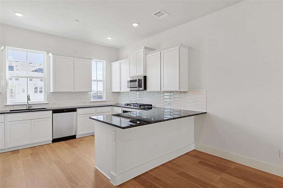 Kitchen featuring light wood-style flooring, white cabinetry, dark stone counters, decorative backsplash, and recessed lighting