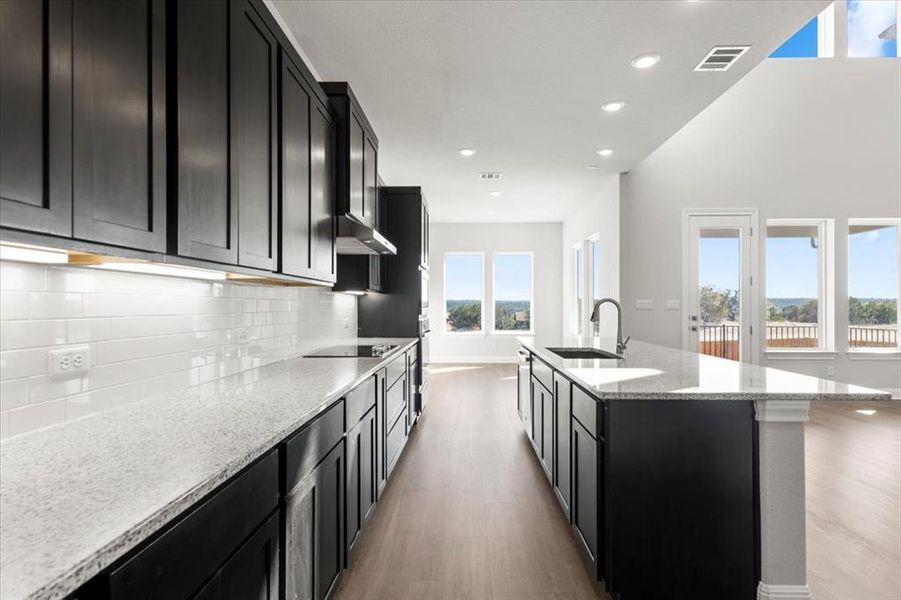 Kitchen with dark cabinets, light stone counters, recessed lighting, light wood-type flooring, and decorative backsplash