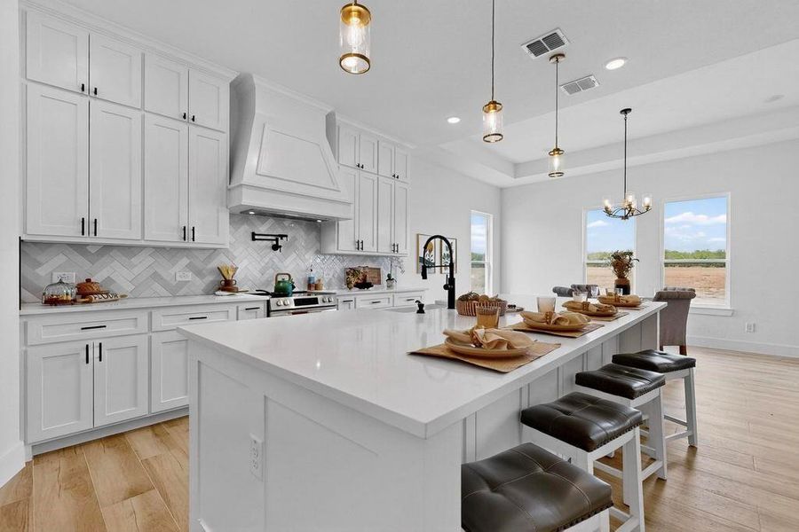 Kitchen with white cabinetry, tasteful backsplash, custom range hood, a raised ceiling, and light wood finished floors Kitchen with white cabinetry, tasteful backsplash, custom range hood, a raised ceiling, and light wood finished floors