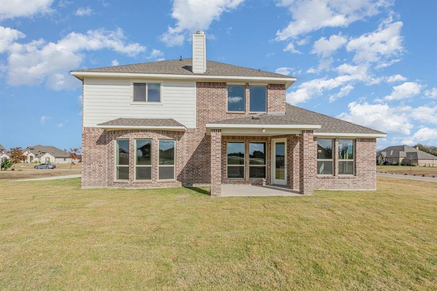 Rear view of house featuring a shingled roof, a yard, brick siding, and a patio