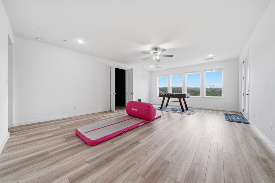 This expansive room features light-toned flooring, white walls, and a ceiling fan with integrated lighting