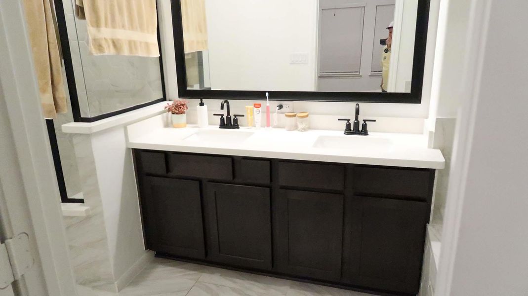 This bathroom features a sleek, modern design with a dark wood vanity, dual sinks, and black fixtures. A large mirror enhances the space, while light-colored tile flooring and walls create a bright, inviting atmosphere. This bathroom features a sleek, modern design with a dark wood vanity, dual sinks, and black fixtures. A large mirror enhances the space, while light-colored tile flooring and walls create a bright, inviting atmosphere.