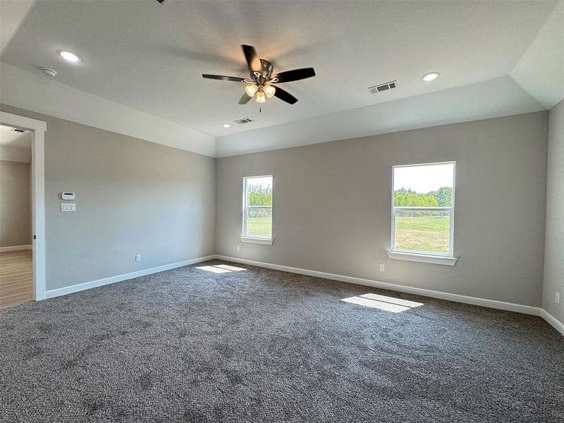 Spacious room featuring gray carpeting, light gray walls, a tray ceiling, recessed lighting, and a ceiling fan