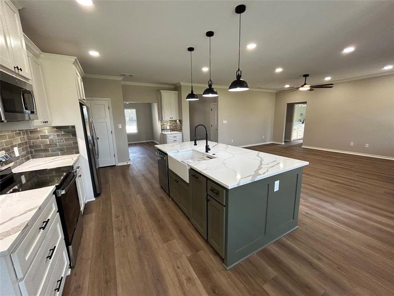 Kitchen featuring backsplash, appliances with stainless steel finishes, white cabinetry, a kitchen island with sink, and pendant lighting