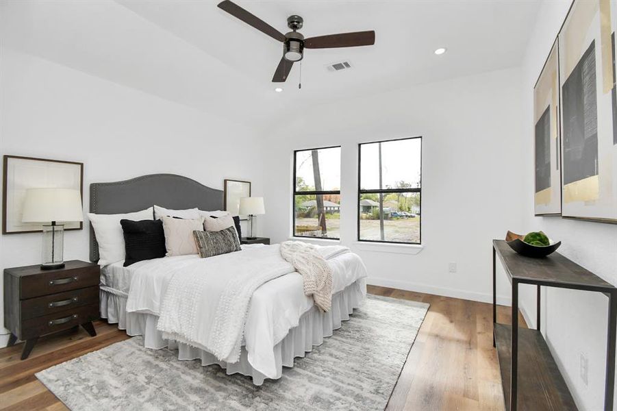 Modern bedroom featuring high ceilings with a ceiling fan, large windows with a view of trees, contemporary decor, and wood flooring.