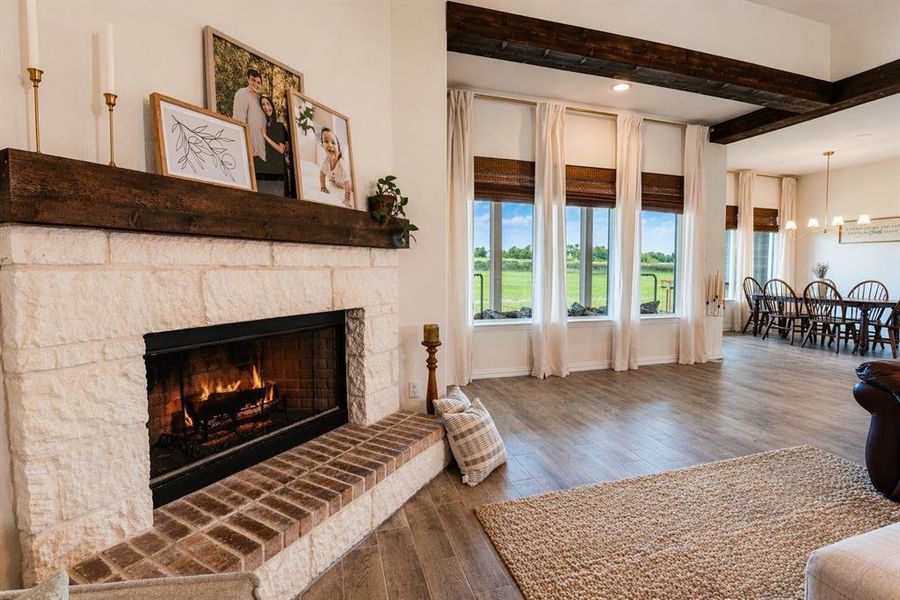 Stone fireplace with a substantial timber mantel, brick hearth, wood-finish flooring, and exposed ceiling beams