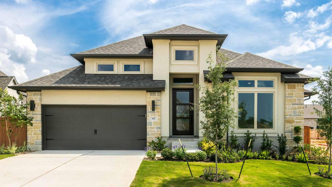 Prairie-style home featuring stucco siding, driveway, a front lawn, and stone siding