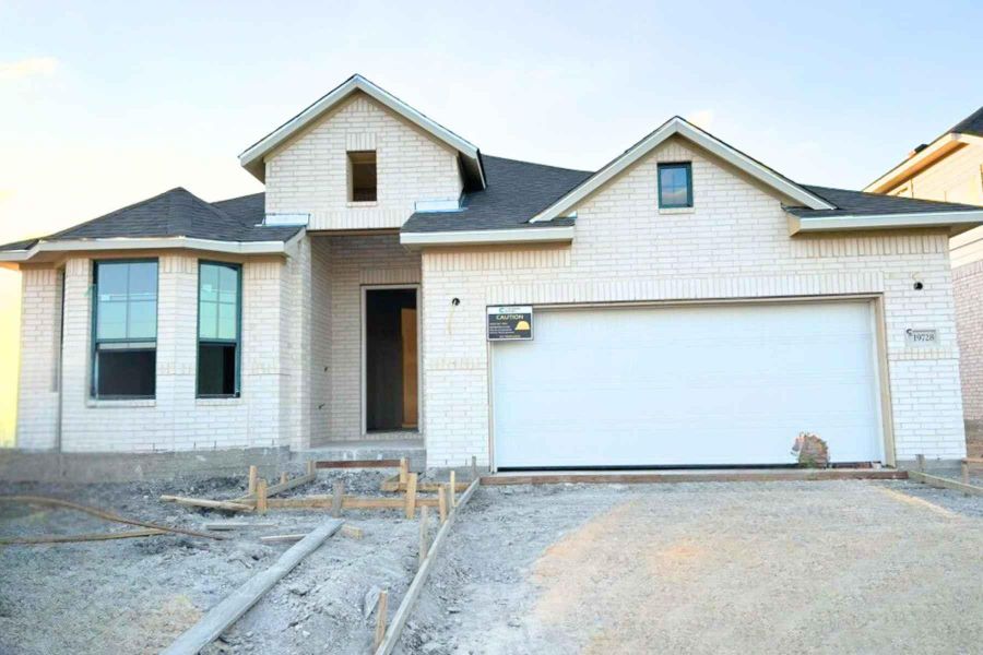 View of front facade with driveway, brick siding, roof with shingles, and an attached garage