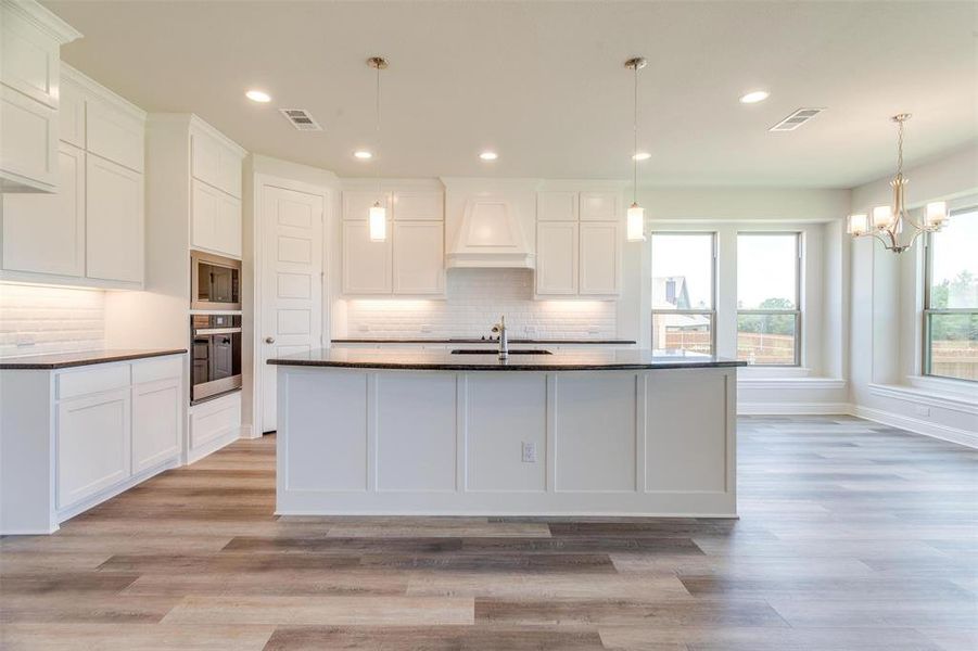 Kitchen featuring backsplash, oven, custom range hood, black microwave, and a kitchen island with sink