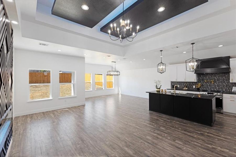 Kitchen featuring a kitchen island with sink, white cabinets, open floor plan, a tray ceiling, and dark countertops