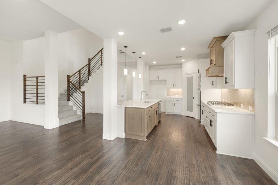 Open-concept kitchen with white cabinets, center island, dark hardwood floors, and staircase in background.