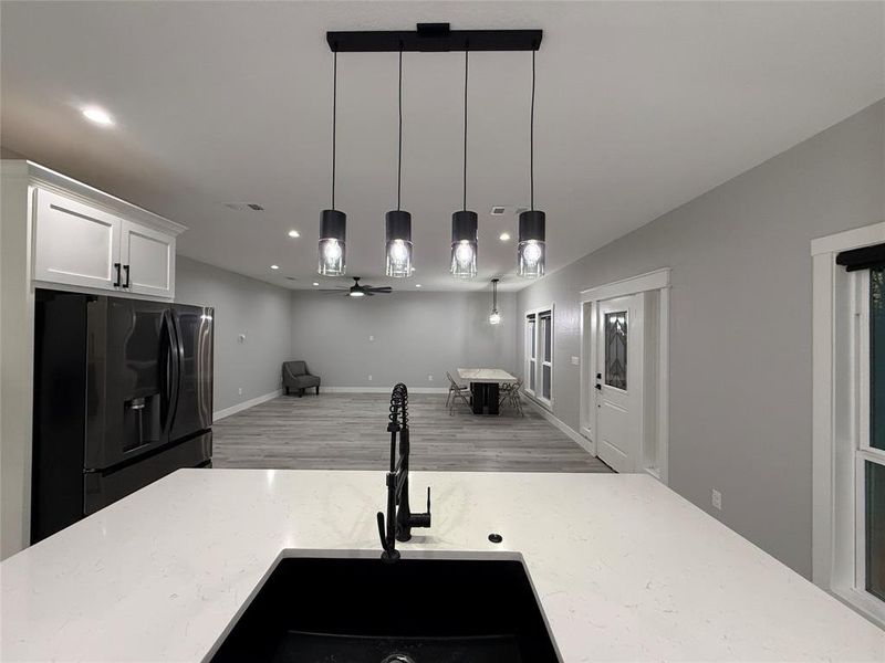 Kitchen featuring black fridge, decorative light fixtures, light stone counters, open floor plan, and white cabinetry