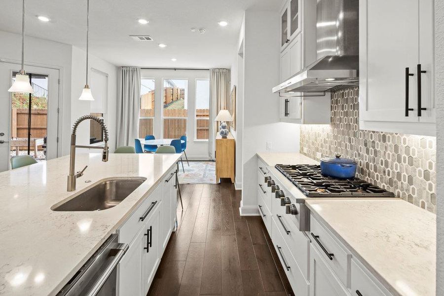 Kitchen featuring a sink, backsplash, wall chimney range hood, dishwashing machine, and dark wood-style flooring