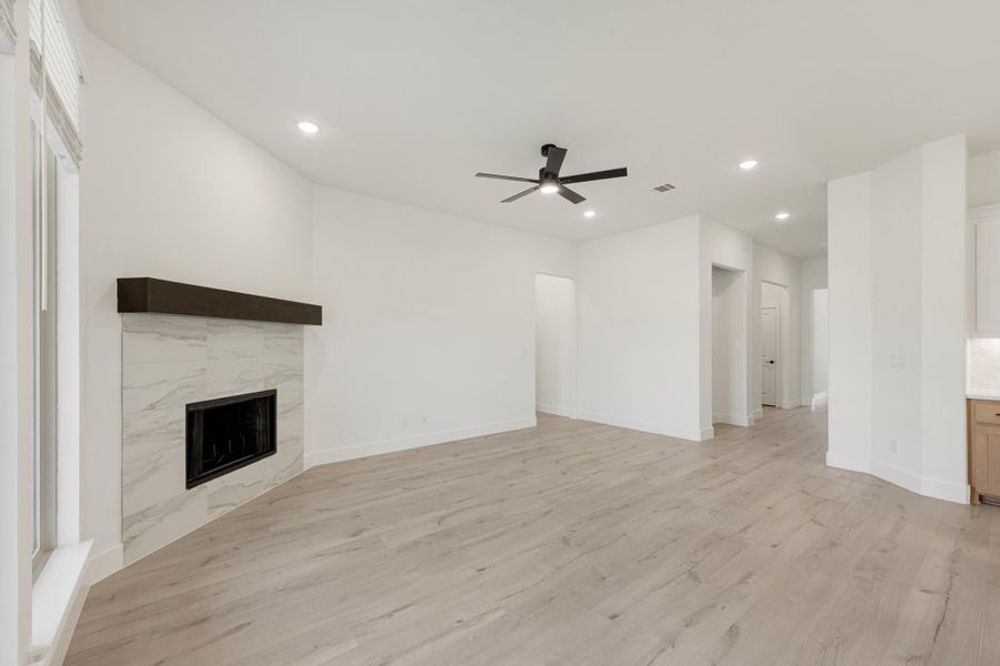 Open living room with marble tile fireplace, ceiling fan, and light hardwood floors