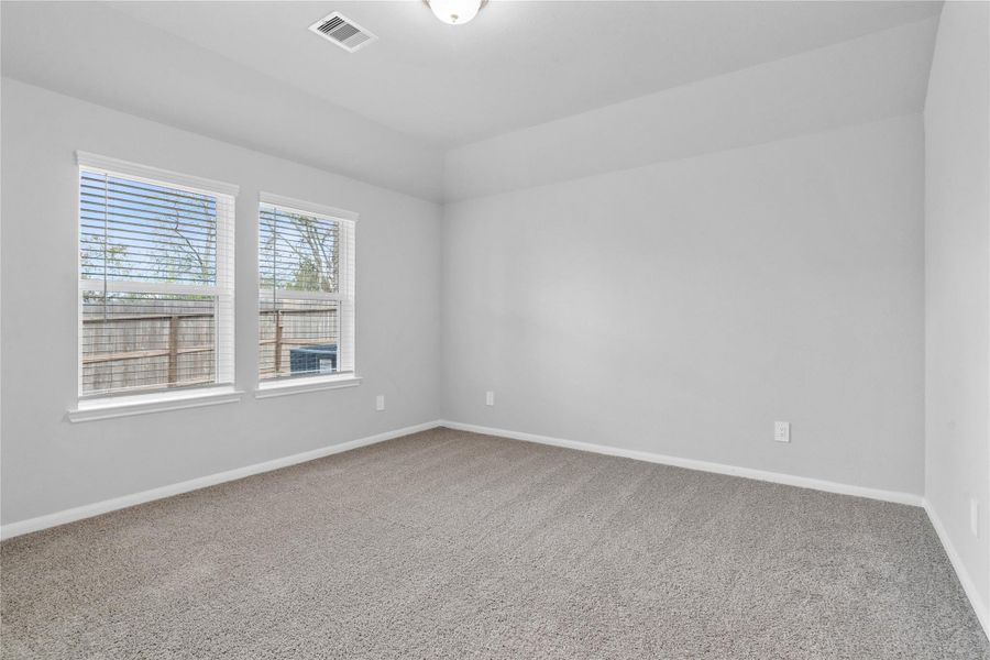The primary bedroom provides a peaceful escape with a bright, neutral palette, sloped ceilings, large windows, and plush carpet flooring, creating a calm and restorative atmosphere to end your day.
