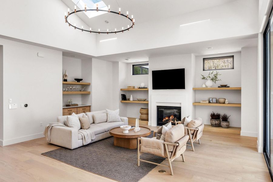 Living area featuring a high ceiling, light wood finished floors, a glass covered fireplace, and suspended lighting