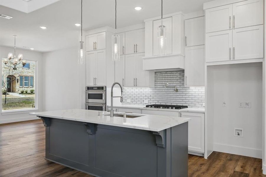 Kitchen featuring an island with sink, a sink, white cabinetry, and pendant lighting