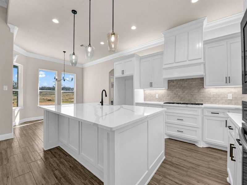 Kitchen with a chandelier, an island with sink, pendant lighting, light stone counters, and white cabinetry