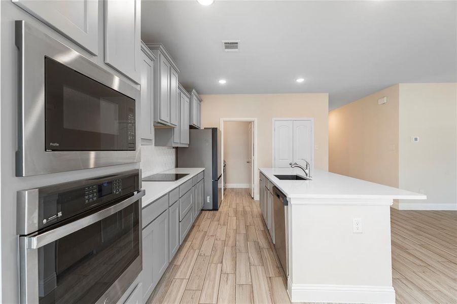 Kitchen with appliances with stainless steel finishes, light countertops, gray cabinets, light wood-style flooring, and recessed lighting