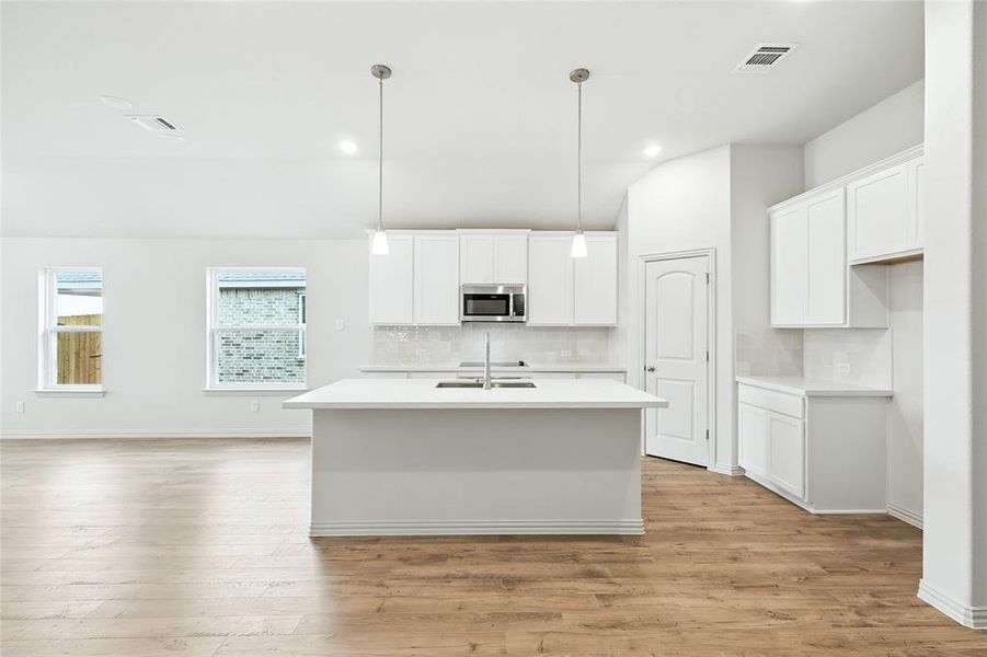 Kitchen featuring decorative backsplash, white cabinetry, an island with sink, light wood-style flooring, and recessed lighting Kitchen featuring decorative backsplash, white cabinetry, an island with sink, light wood-style flooring, and recessed lighting