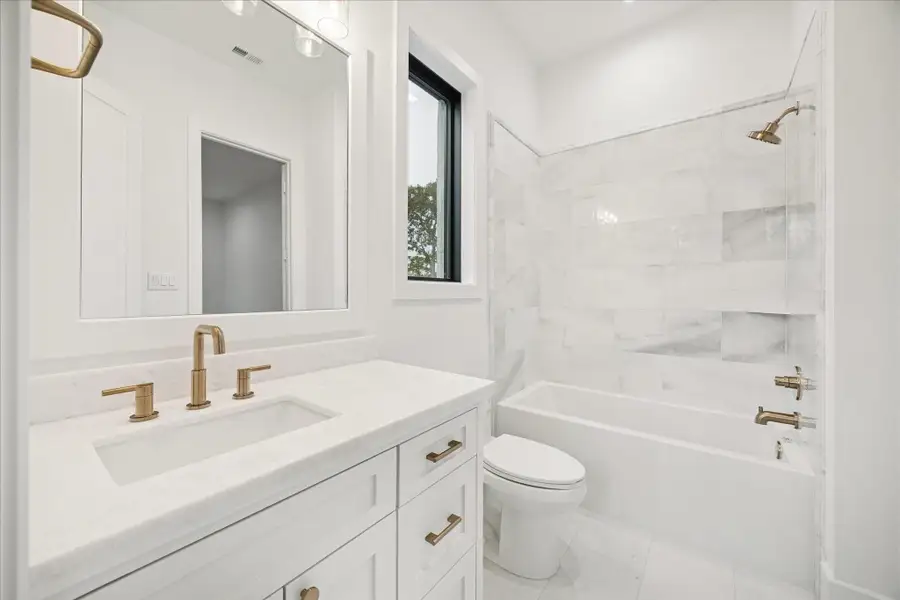 Marble-inspired tile, warm brass hardware, and a crisp white vanity define the secondary en-suite bath with clean, refined simplicity.