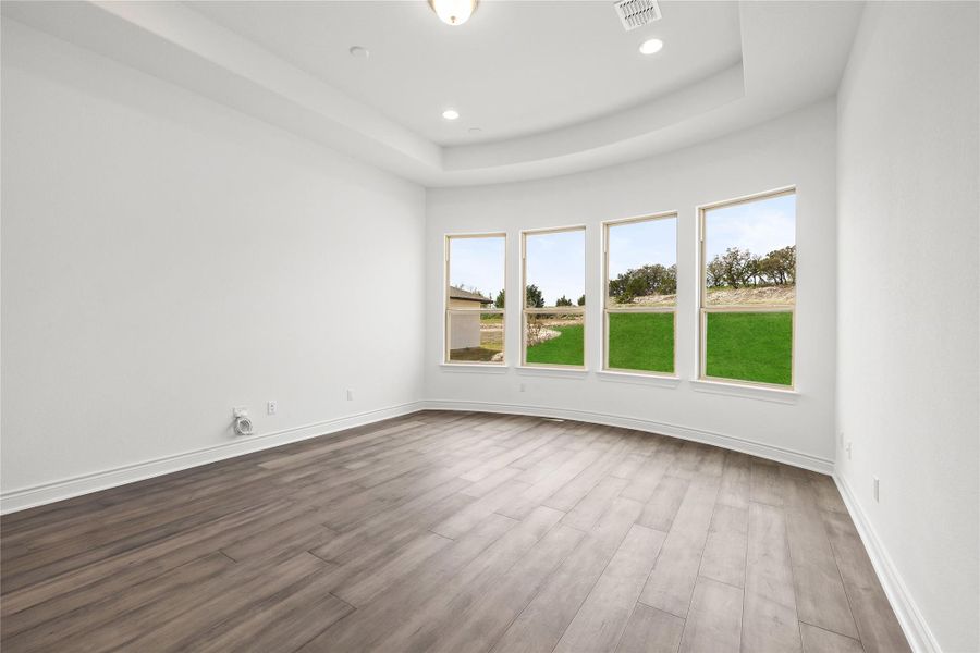 Empty room with a tray ceiling, dark wood-style floors, and recessed lighting