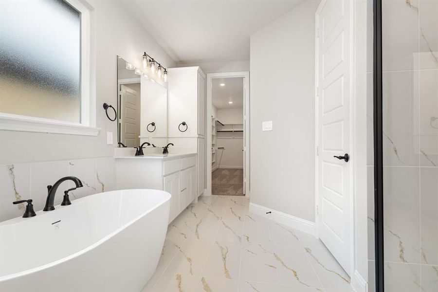 Full bathroom with double vanity, a freestanding tub, a spacious closet, and light marble finish floors