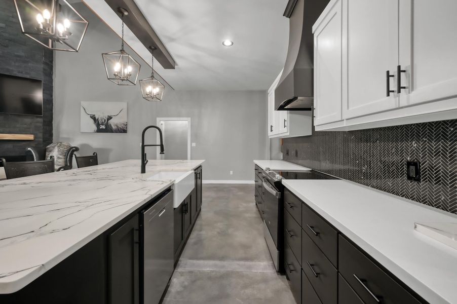This modern kitchen features sleek black and white cabinetry, a spacious marble countertop island with a farmhouse sink, and stylish geometric pendant lighting. The herringbone backsplash adds a touch of elegance, while the open layout offers ample space for entertaining.