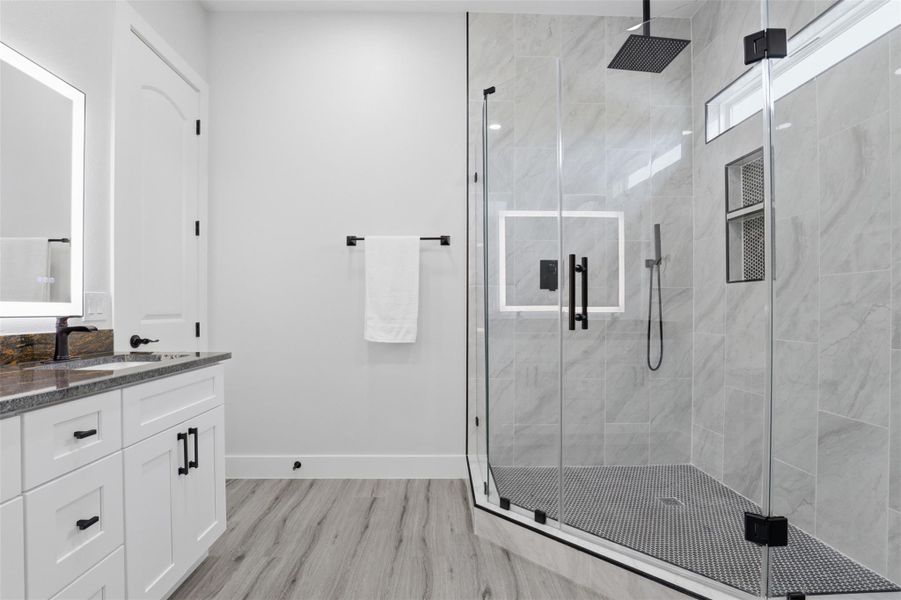 Spacious walk-in shower with clear glass enclosure and black hardware, complemented by light grey marble-style tiled walls and a black mosaic tile floor