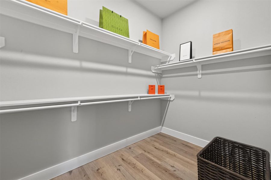 Spacious walk-in closet designed for both function and style, offering custom shelving, abundant hanging space, and durable white oak–finish laminate flooring—perfect for an organized, boutique-style wardrobe experience.