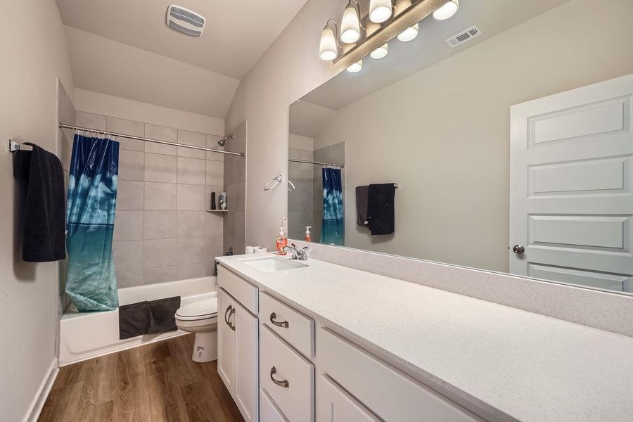 Full bath featuring visible vents, toilet, shower / bath combo, vanity, and wood finished floors