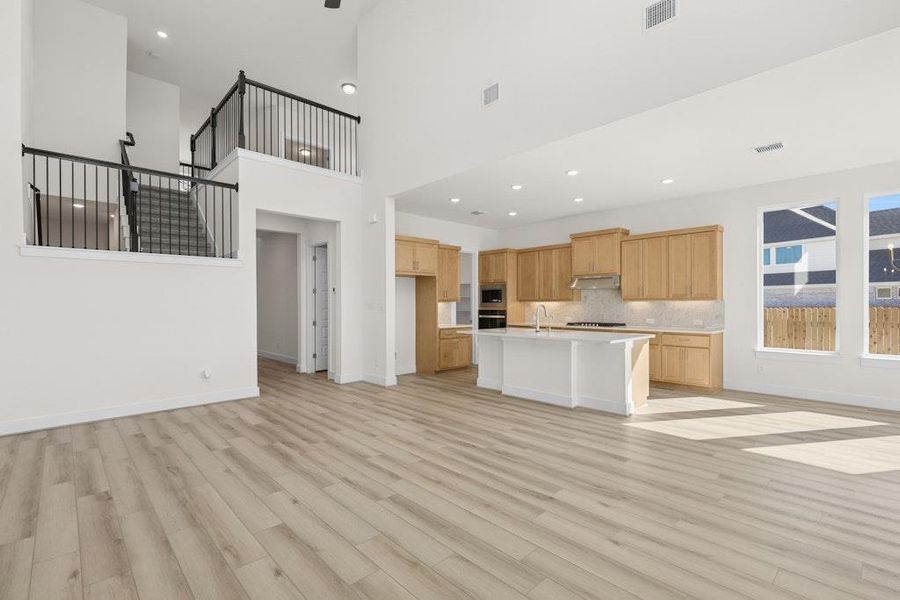 Kitchen featuring open floor plan, a high ceiling, light wood-type flooring, a breakfast bar, and a kitchen island with sink Kitchen featuring open floor plan, a high ceiling, light wood-type flooring, a breakfast bar, and a kitchen island with sink