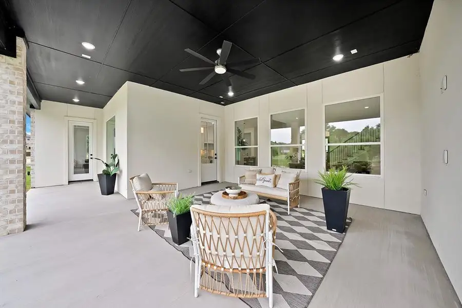 Covered patio featuring a dark-toned ceiling with recessed lighting and a ceiling fan, light-colored concrete flooring, and multiple large windows