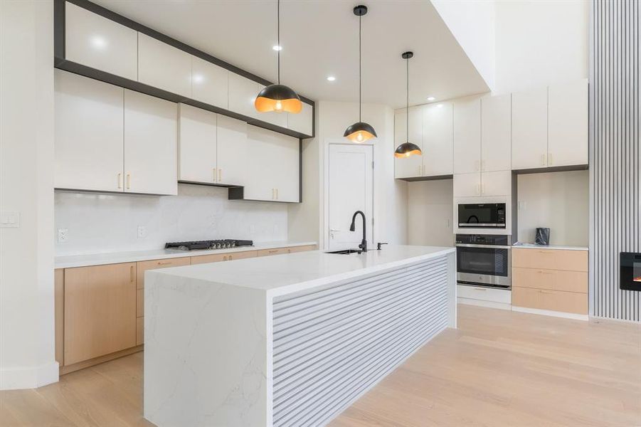 Kitchen featuring hanging light fixtures, white cabinetry, stainless steel appliances, light stone counters, and a center island with sink Kitchen featuring hanging light fixtures, white cabinetry, stainless steel appliances, light stone counters, and a center island with sink