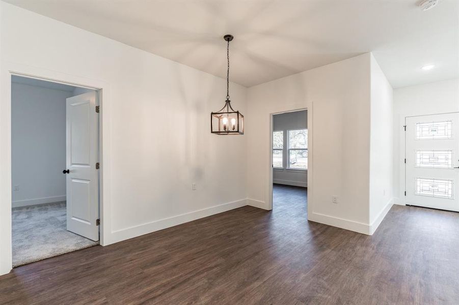 Unfurnished dining area featuring dark wood-type flooring and a notable chandelier