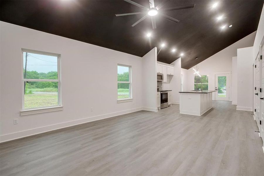 Unfurnished living room featuring high vaulted ceiling, ceiling fan, and light wood-style floors