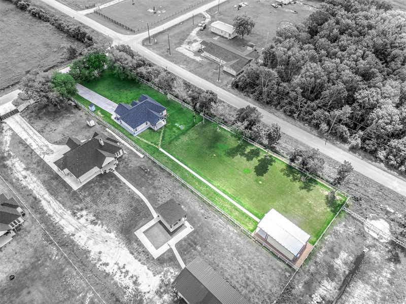 This aerial perspective showcases the full layout of the property, including the main residence, expansive lawn, fenced areas, and additional outbuilding. The setting offers a great combination of privacy, usable outdoor space, and convenient access along a quiet roadway.