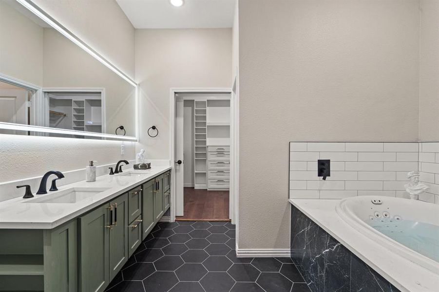 Full bath featuring a tub with jets, double vanity, dark tile patterned flooring, a spacious closet, and a textured wall Full bath featuring a tub with jets, double vanity, dark tile patterned flooring, a spacious closet, and a textured wall