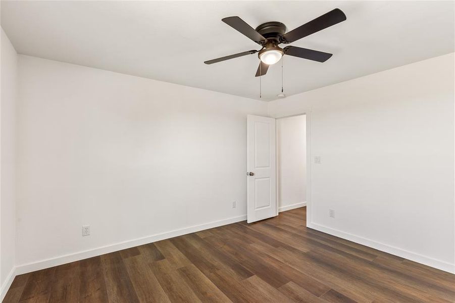 Room featuring wood-finish flooring, white baseboards, a white interior door, and a ceiling fan with integrated lighting