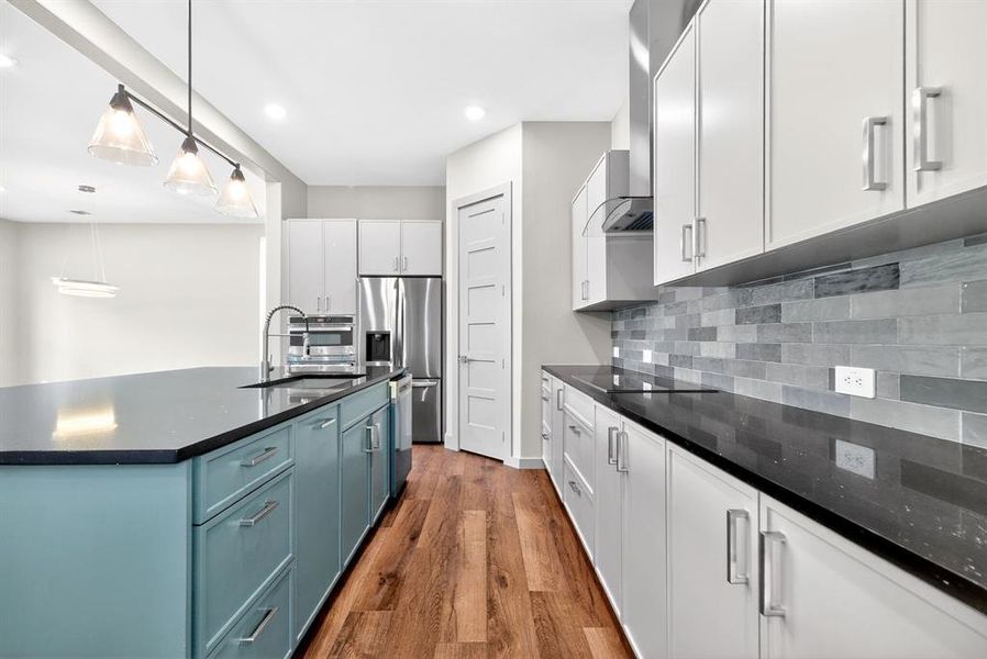 Two tone kitchen featuring dark wood-style floors, stainless steel appliances, an island with sink, decorative light fixtures, and dark stone counters Two tone kitchen featuring dark wood-style floors, stainless steel appliances, an island with sink, decorative light fixtures, and dark stone counters