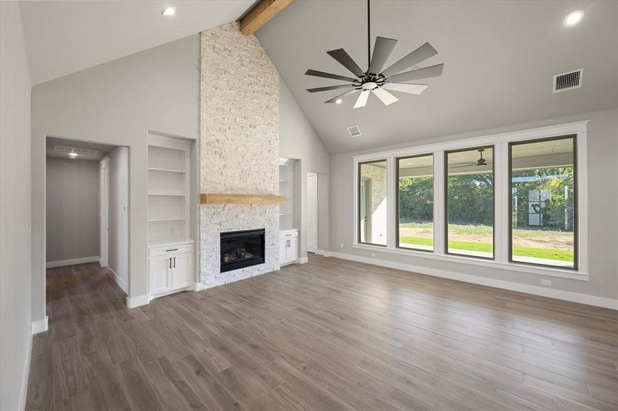 Living room featuring a vaulted ceiling with a beam, built-in shelves & cabinets, ceiling fan, and a stone gas fireplace