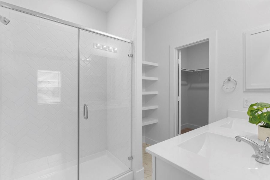 Luxurious primary bath featuring a sleek large glass-enclosed shower, dual vanities with modern fixtures, built-in shelving, and direct access to an expansive walk-in closet for organized storage.