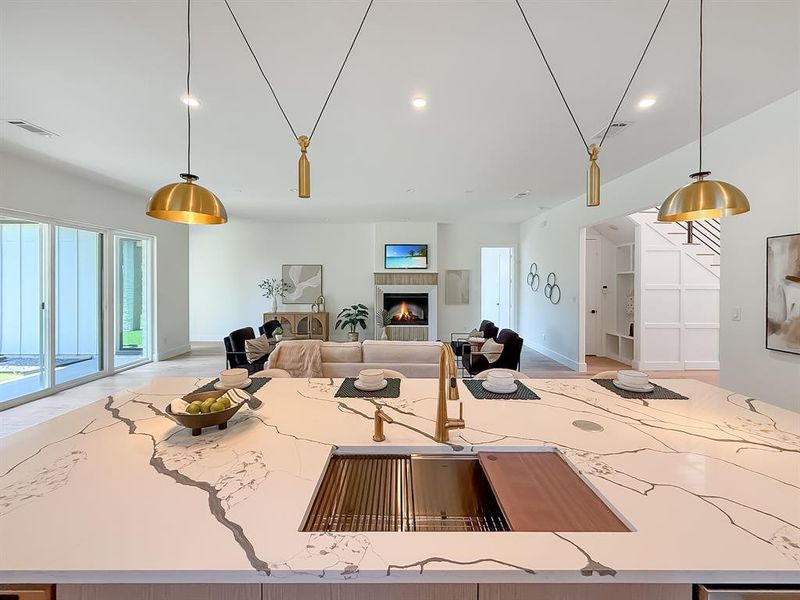 Kitchen featuring pendant lighting, light stone counters, a lit fireplace, open floor plan, and a center island with sink Kitchen featuring pendant lighting, light stone counters, a lit fireplace, open floor plan, and a center island with sink