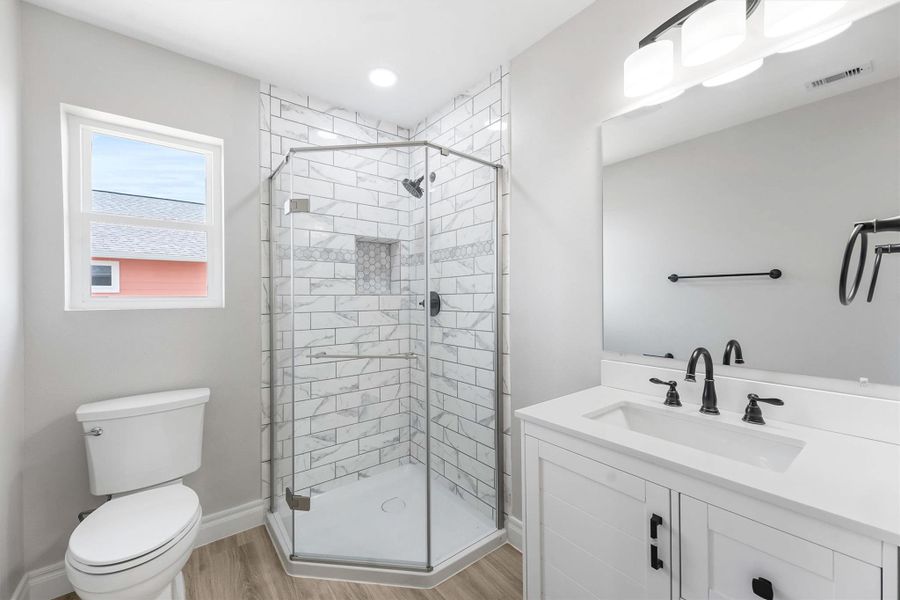 This bathroom features a modern design with a glass-enclosed corner shower, sleek white vanity, and matte black fixtures. The space is brightened by natural light from a window and complemented by light wood flooring. This bathroom features a modern design with a glass-enclosed corner shower, sleek white vanity, and matte black fixtures. The space is brightened by natural light from a window and complemented by light wood flooring.