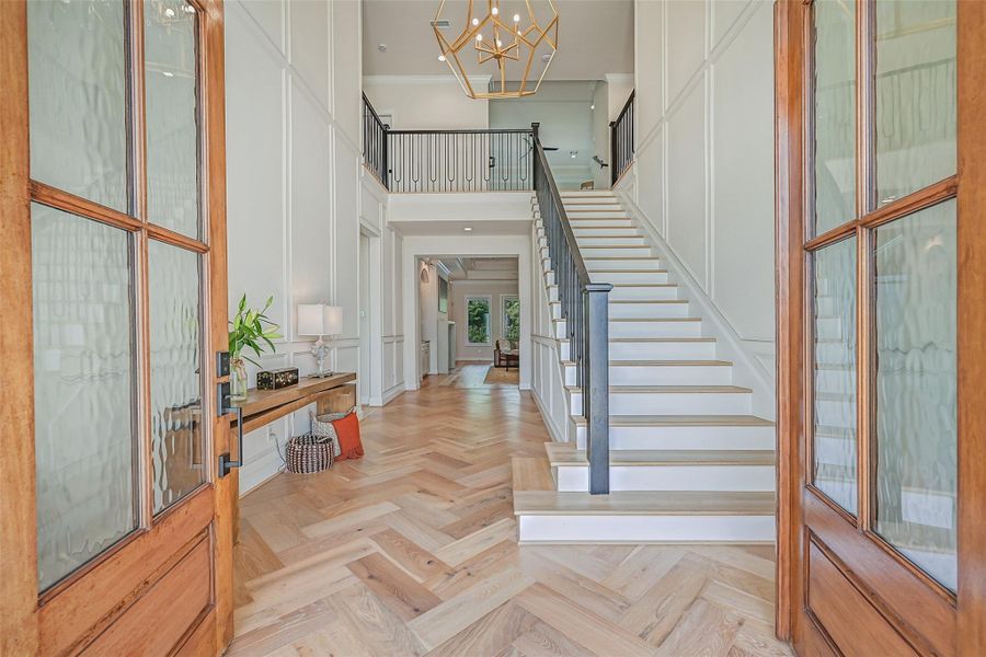 Step inside to a dramatic 20' foyer showcasing beautiful herringbone wood-look tile, extensive custom millwork, a statement chandelier & open staircase with contemporary iron railing.