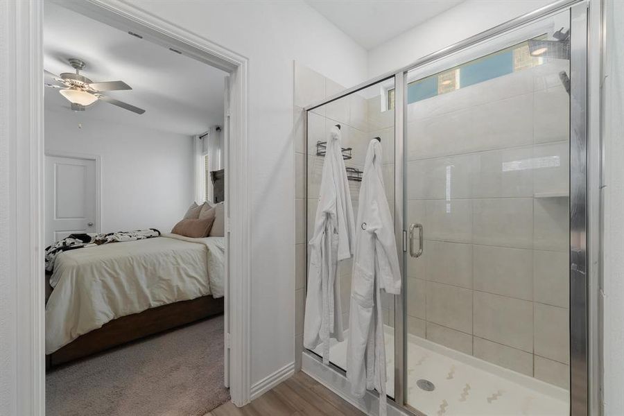 Bathroom with hardwood / wood-style floors, ceiling fan, plenty of natural light, and a shower with door